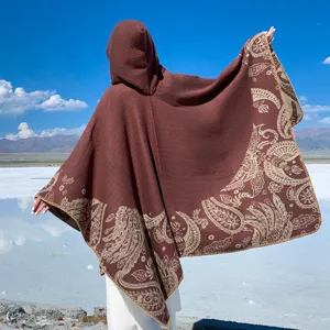 Detailed back view of a thick brown hooded knit poncho with beige paisley patterns in nature