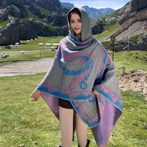 Modische Frau trägt einen dicken Kapuzenschal mit Phönixmuster in einer Berglandschaft
