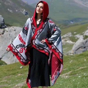 Elegante Frau mit rot-grauem Kapuzenponcho mit Muster in den Bergen im Freien