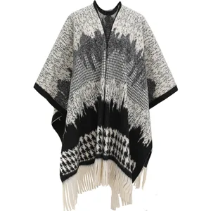 Detailed view of the classic houndstooth pattern and white tassel fringe on this knit poncho