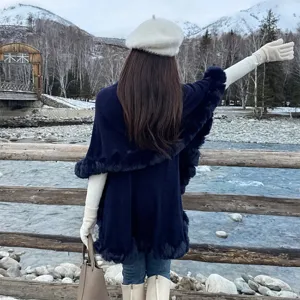 Detailed back view of a stylish navy blue knit poncho with faux fur trim in winter scenery