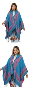 Détail d'un poncho en tricot bleu à capuche avec motifs de cœurs et franges noires.