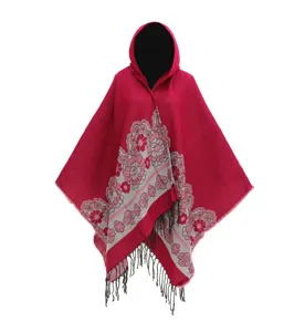 Detalle del poncho rojo con capucha, flores tejidas y borlas negras decorativas.