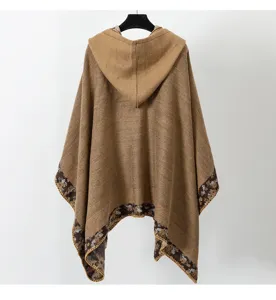 Vista trasera de un poncho tejido bohemio marrón con capucha y borde de flores en percha