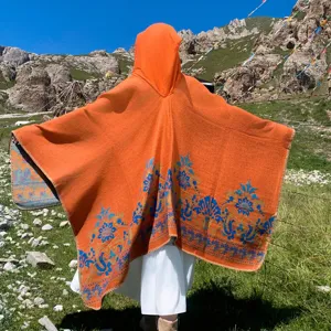Back view of orange knitted hooded poncho with blue floral jacquard on green hills