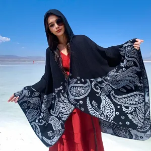 Detailed view of black paisley hooded knitted poncho cape against a clear blue sky