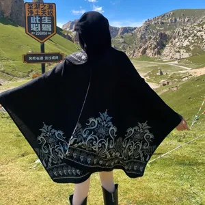 Detail of black hooded knit poncho with vintage jacquard pattern in mountain landscape