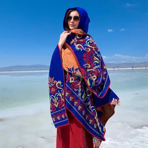 Outdoor detail of a hooded jacquard shawl with vibrant floral patterns under a blue sky