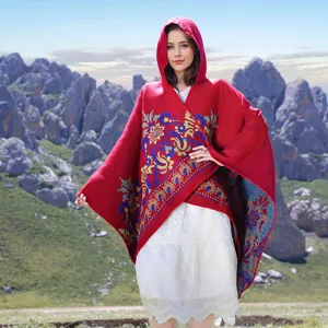 Detailed view of a red hooded knit poncho with vintage floral jacquard pattern outdoors.