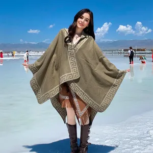 Model wearing a hooded olive knit poncho with fringe and Greek key pattern at a salt lake.