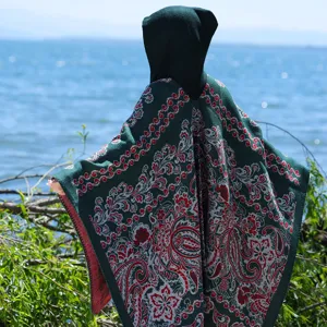 Detail eines gestrickten Kapuzenponchos mit rotem Paisley-Blumenmuster in Dunkelgrün
