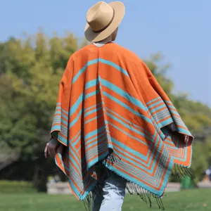 Back view of men's orange and teal striped knitted poncho with fringe in outdoor setting