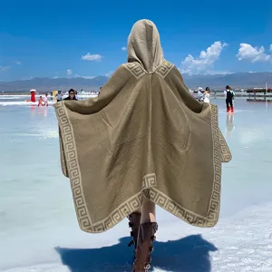 Back view of a warm hooded knitted travel poncho featuring a classic Greek key pattern border
