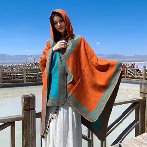 Detail view of a stylish bohemian hooded knit poncho in orange with teal fret patterns