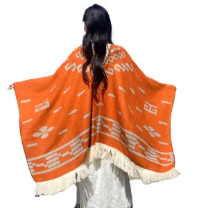 Rückansicht eines orangefarbenen Strickponchos mit weißen geometrischen Mustern und Fransen