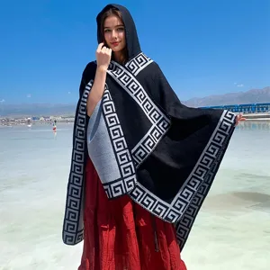 Elegant hooded knit poncho with Greek key pattern worn by a model in a scenic travel setting