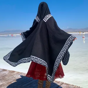 Back view of black hooded knit poncho with Greek key pattern in a scenic travel setting
