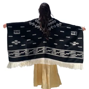 Detailansicht eines schwarzen Strick-Ponchos mit geometrischem Muster und weißen Fransen.