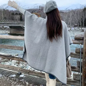 Πίσω όψη γυναίκας που φοράει γκρι χειμωνιάτικο πόντσο σε χιονισμένο ορεινό τοπίο