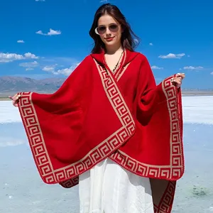 Detail view of red knitted hooded poncho with elegant gold Greek key pattern trim