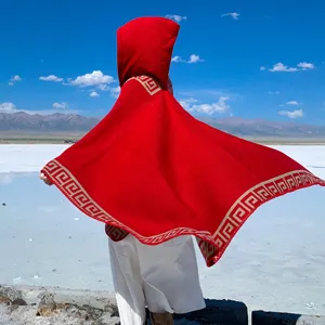 Detail of a red hooded knit poncho with Greek key pattern border against a bright sky.