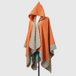 Detailed view of orange knitted hooded poncho with blue Greek key pattern border