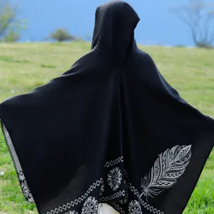 Rückansicht eines schwarzen Kapuzenponchos mit weißem Feder- und Stammesmuster im Freien.