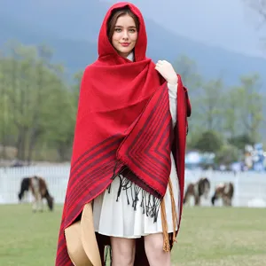 Model wearing red and black striped hooded knit shawl with fringe in outdoor setting
