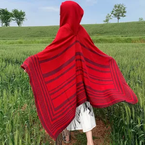 Detailed back view of a red hooded knit striped poncho cape with fringe in nature