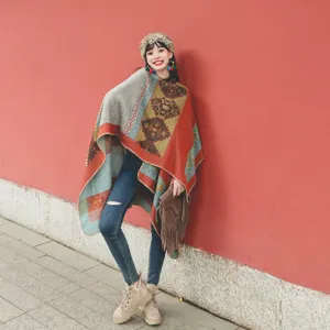 Asian model posing in ethnic style retro patterned warm poncho shawl against red wall