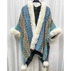 Detailansicht eines ethnischen blauen Strickponchos mit Kunstpelzkragen und weichen Pompons.
