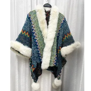 Detailansicht eines ethnischen Strickponchos mit weißem Kunstfellkragen und Pompons