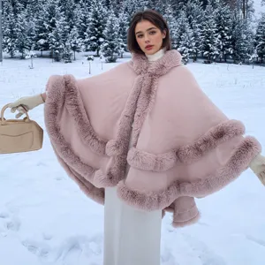 Poncho en maille rose élégant avec bordure en fausse fourrure, porté dans une scène de neige.