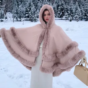 Poncho en maille rose à capuche avec bordure en fourrure dans un paysage de neige