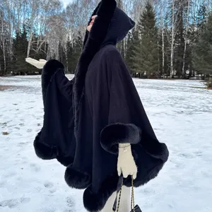 Détail d'un poncho en maille noire à capuche avec bordure en fausse fourrure dans la neige.