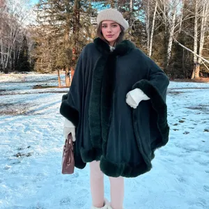 Poncho en tricot vert foncé élégant avec bordure en fausse fourrure dans la neige.