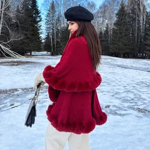 Elegant red double-layered knit cape with faux fur trim shown in a snowy landscape