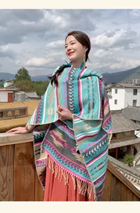 Model im ethnischen Strick-Poncho mit Fransen in einem malerischen Bergdorf.