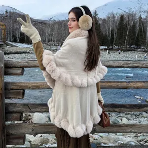 Elegant beige knitted winter poncho with soft faux fur trim shown in a snowy landscape