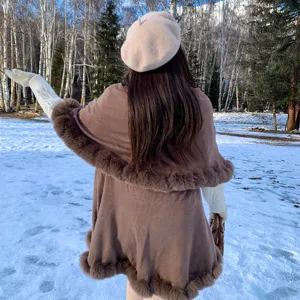 Back view of elegant brown double-layer knit cape with faux fur trim in a snowy forest