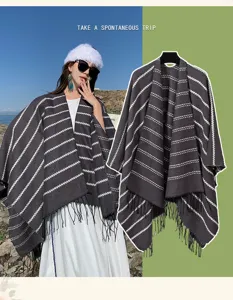 Detail of a grey striped knit shawl with tassels shown in outdoor travel setting