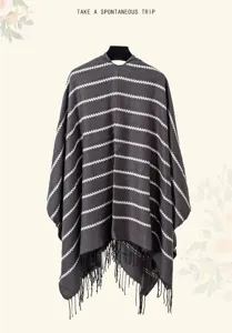 Close-up of a grey and white striped knitted poncho with tassel detailing for travel.