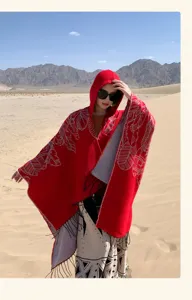 Vibrant red hooded ethnic poncho with fringe detail shown in a desert travel setting.
