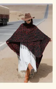 Full-length view of a leopard print knit poncho with tassels on a desert road scene