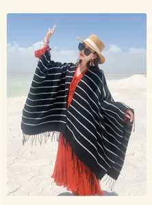 Ethnic style striped knit poncho with fringe details worn by a model in a beach setting