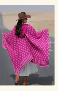 Back view of model wearing a vibrant magenta ethnic style knitted hooded poncho in desert