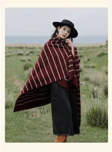 Model wearing a thick red striped knitted poncho with tassels in a natural field