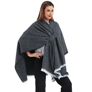 Close-up detail of a grey knit poncho featuring a stylish buckle and white fringe edges.
