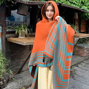 Woman wearing orange and blue striped hooded knit shawl with tassels in outdoor setting