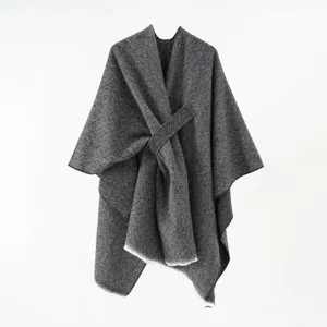 Detailed view of the gray knit poncho featuring a unique diagonal strap and fringe edges